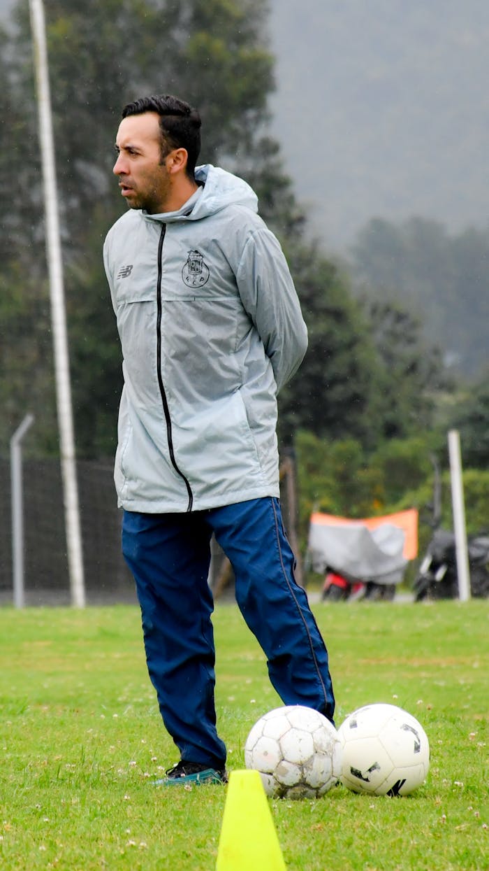 about-img Soccer coach on field with training balls, wearing sportswear and observing.