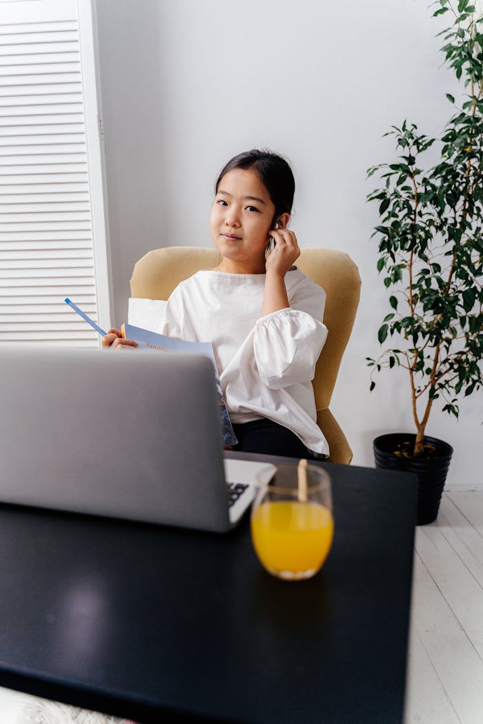 ours-journey Young Asian girl engaged in online learning at home with a laptop and headphones.